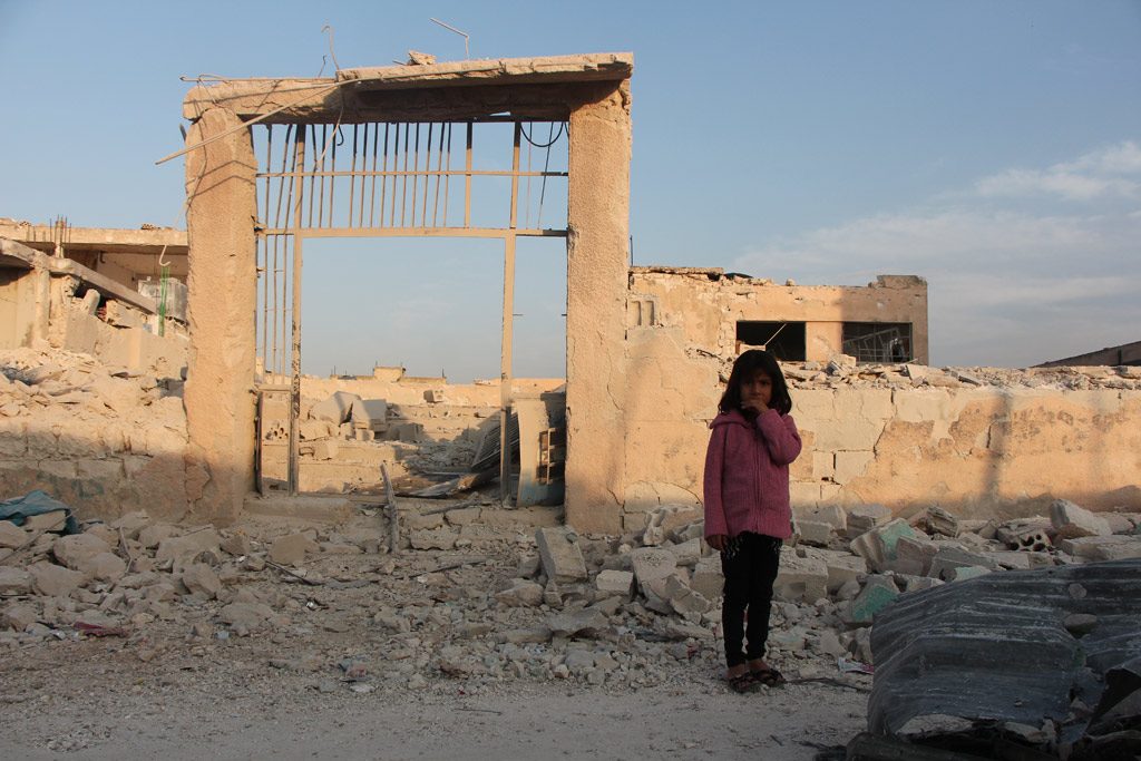 A seven-year-old child stands in front of her damaged school in Idleb, Syria. October 2016. Photo: UNICEF